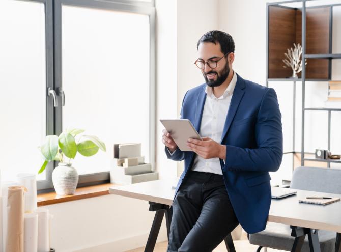 Businessman leaning against desk looking at tablet