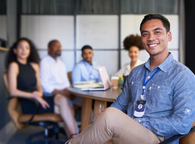 Businessman sitting at table smiling with colleagues in background