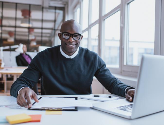 Young man at his desk with laptop doing paperwork.